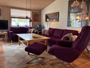 Uma sala de estar com um sofá roxo, uma mesa de centro de madeira e uma televisão em um móvel de madeira.