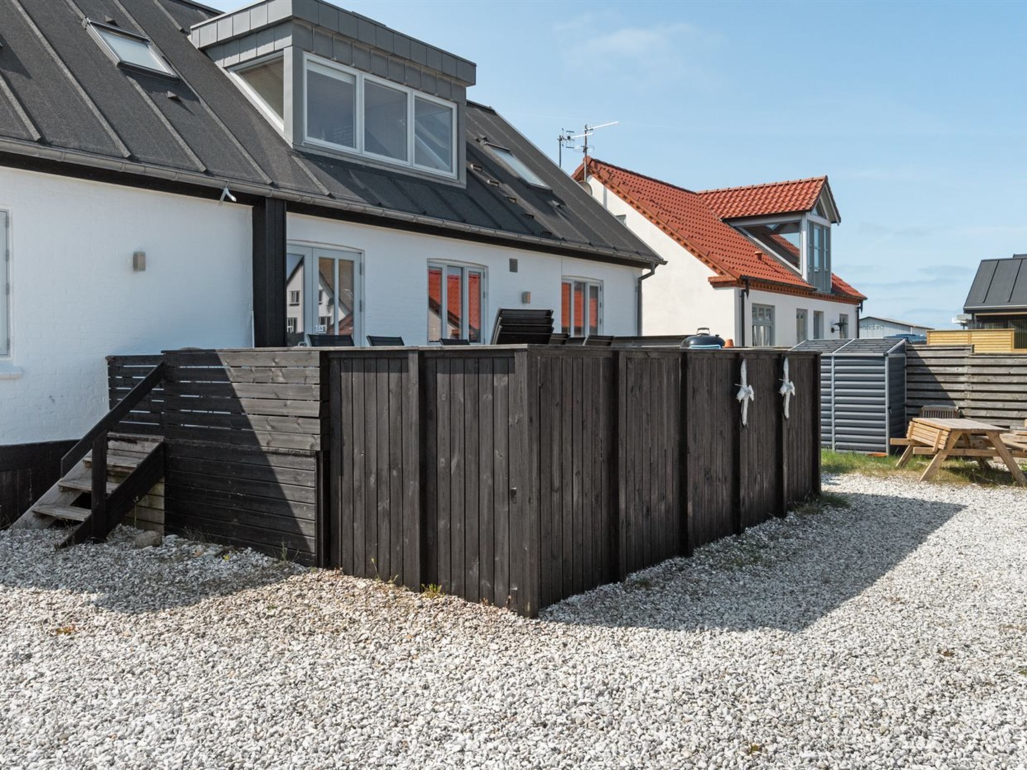 Een woonhuis met een schuin dak, houten omheining en een grindpad.