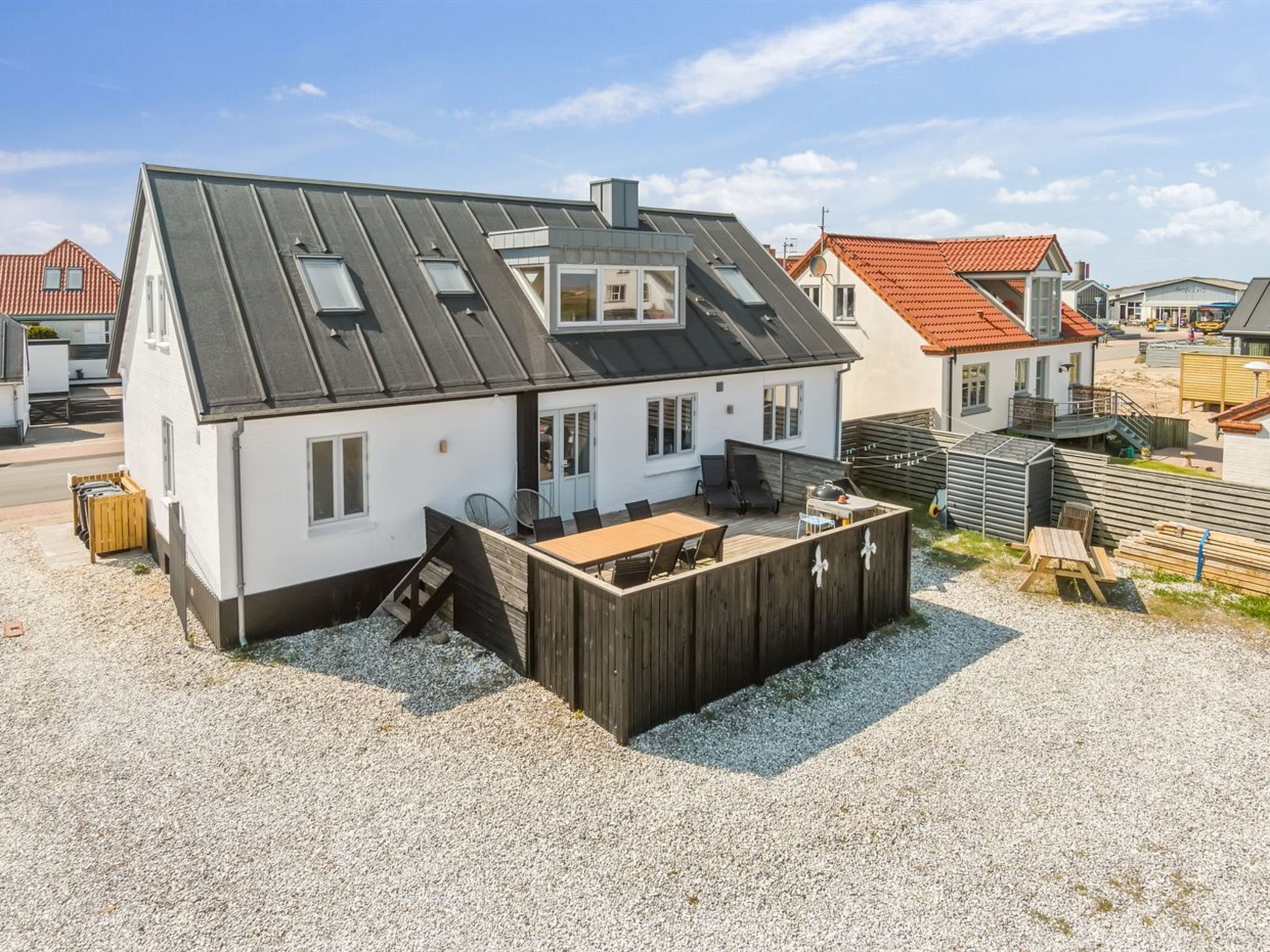 A house with a sloped roof, a patio with outdoor furniture, and a gravel driveway.
