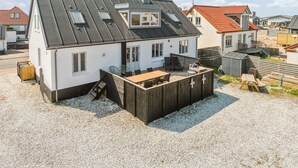 Una casa con techo inclinado, un patio con mobiliario exterior y un camino de entrada de grava.