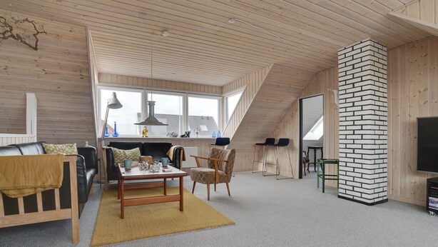 Un loft amplio con techo alto, vigas de madera, pared de ladrillo y un gran ventanal que proporciona luz natural.
