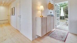 A modern interior with a wooden floor, a white wall, a wooden cabinet, a lamp, and a view of the outdoors.