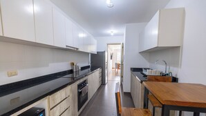 A modern kitchen with white cabinets, a black countertop, and a wooden dining table. - 3BedRoom APT in the HEART of BARRANCO, LIMA, PERU 🇵🇪 (Barranco)