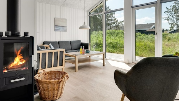 A modern living room with a wood-burning stove, a sofa, a coffee table, and large windows offering a view of greenery outside. - "Raakel" - 950m from the sea by Interhome (Thisted)