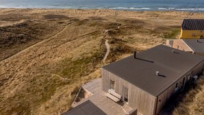 A coastal property with a wooden deck, a modern building with a dark roof, and a sandy beach in the background.