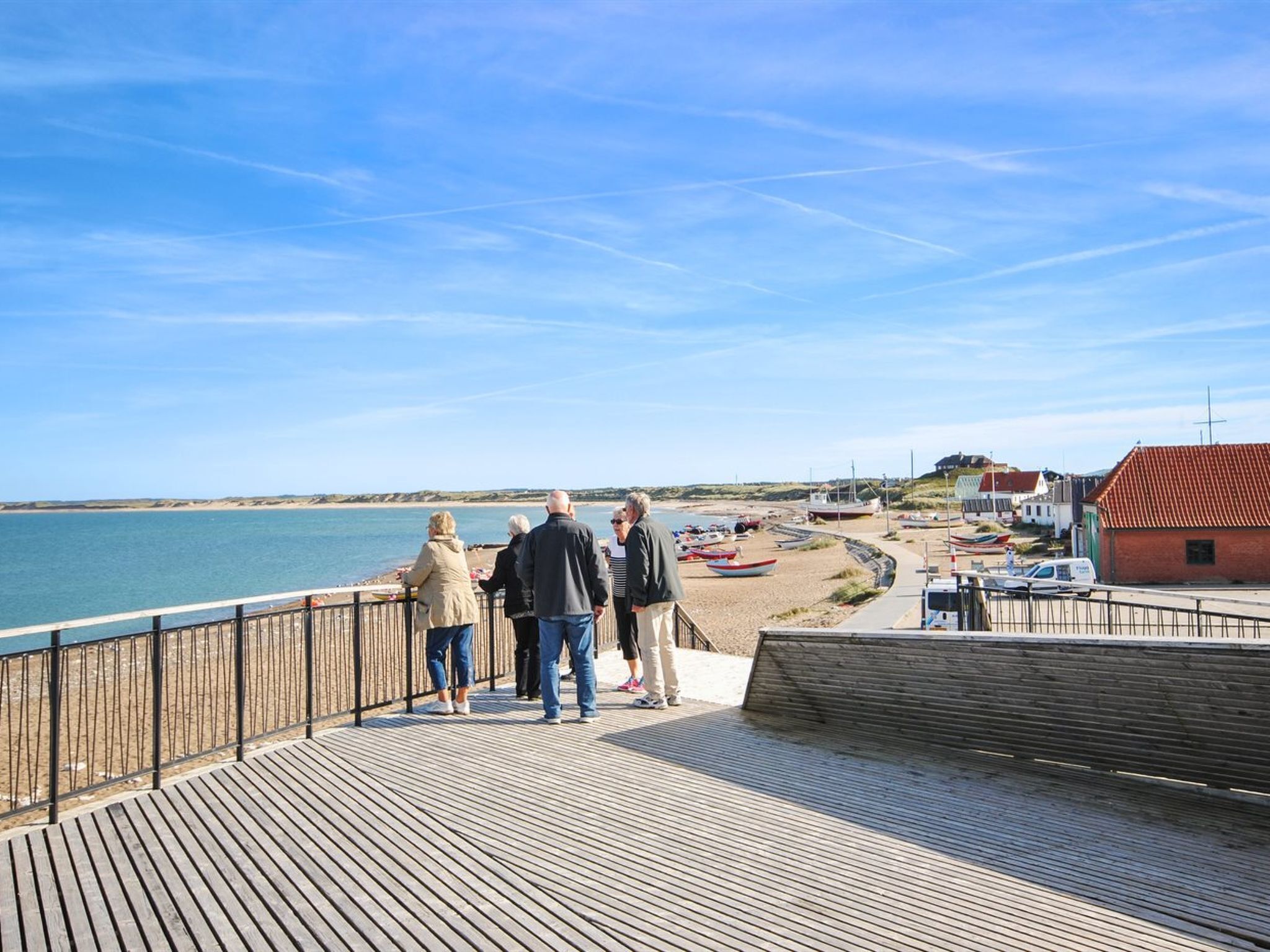 Une jetée en bois où se tiennent des personnes qui observent la plage.