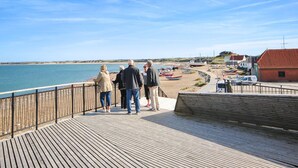 A wooden pier with people standing and looking at the beach.
