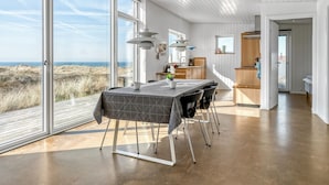 A modern kitchen with white cabinets, a dining area with a table and chairs, and large windows offering a view of the beach.