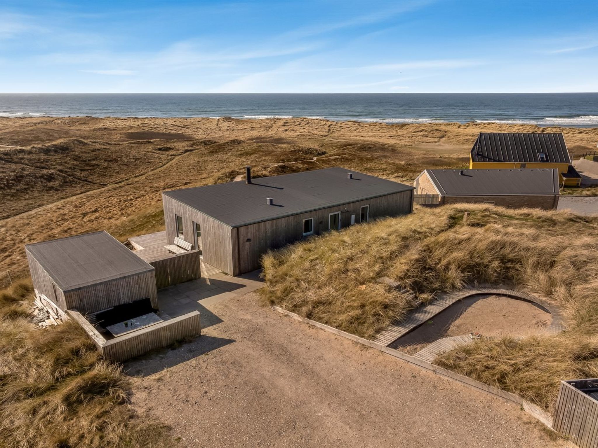 Ein modernes Haus mit flachem Dach, gelegen auf sandigem Gelände mit Blick auf den Ozean.