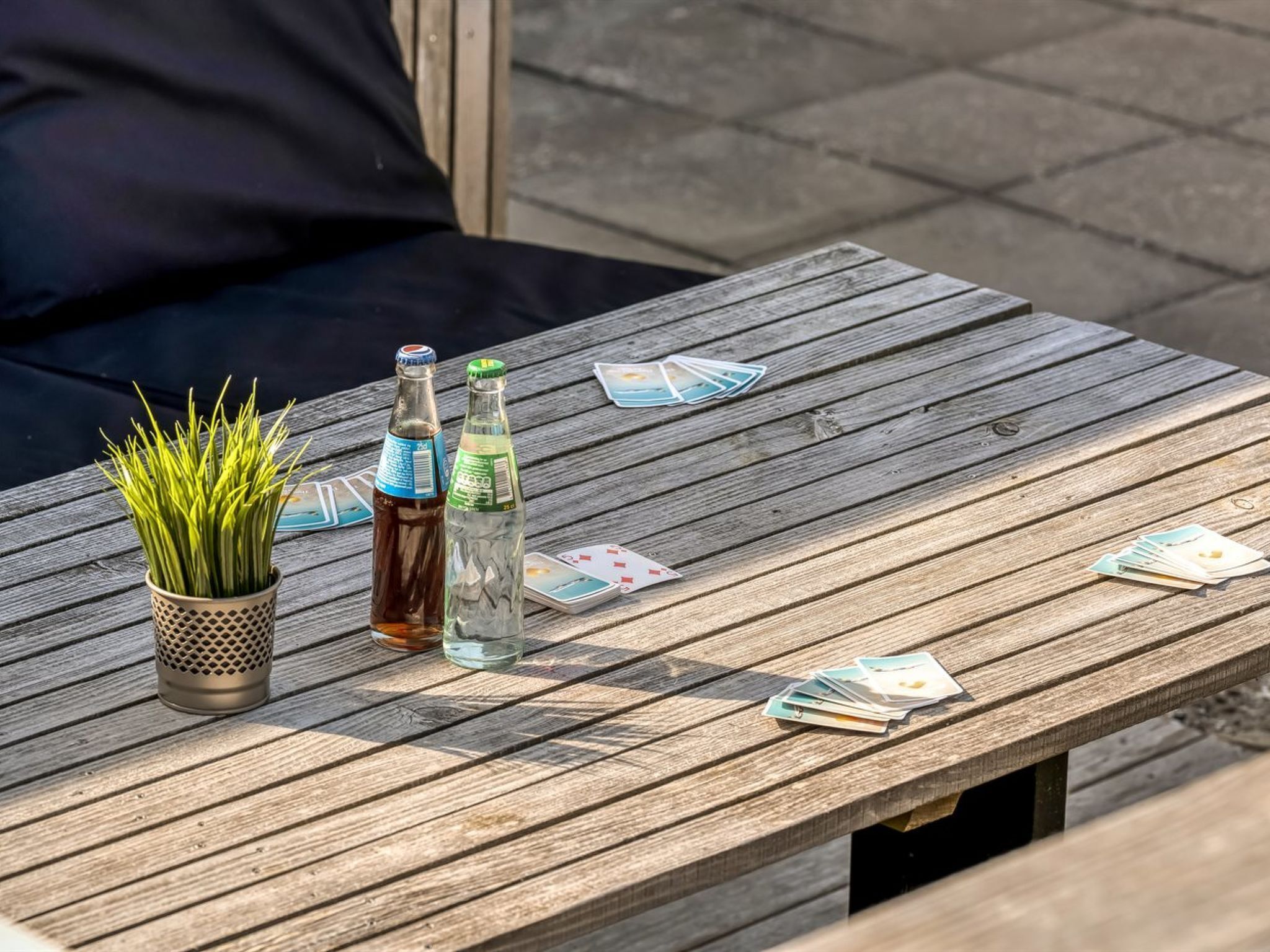 Una mesa de madera con una planta en maceta, dos botellas y cartas.