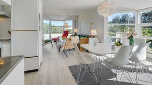 Et lyst, åbent køkken- og spiseområde med hvide skabe, et stort vindue og et loft med et unikt, fjerlignende design.