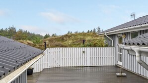 Une terrasse sur le toit, dotée d’un plancher en bois, entourée d’une clôture blanche et offrant une vue sur un paysage vallonné.