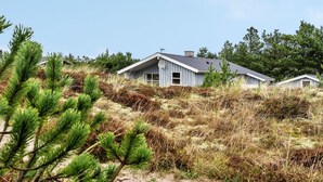 Une maison dotée d’un toit à pignon, entourée d’une végétation naturelle et d’arbres.