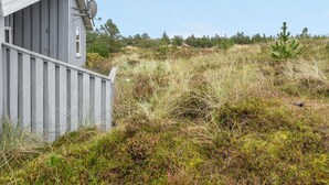 Un petit bâtiment d’un seul étage, doté d’un toit en pente et d’une antenne parabolique, entouré de hautes herbes et de quelques arbres clairsemés.