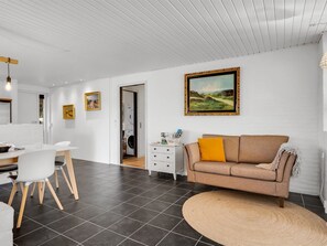 A modern living room with a sofa, a dining table with chairs, a white dresser, and a painting on the wall. - "Örjan" - 400m from the sea by Interhome (Thisted)