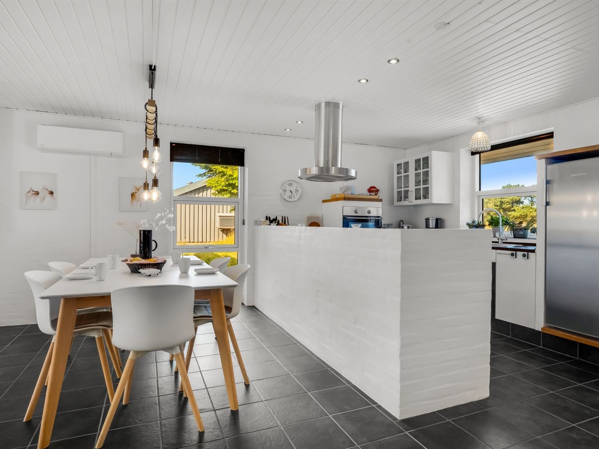 A modern kitchen with a central island, white cabinetry, and a dining area with a white table and chairs.