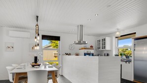 Een moderne keuken met een centraal eiland, witte kasten en een eethoek met een witte tafel en stoelen.
