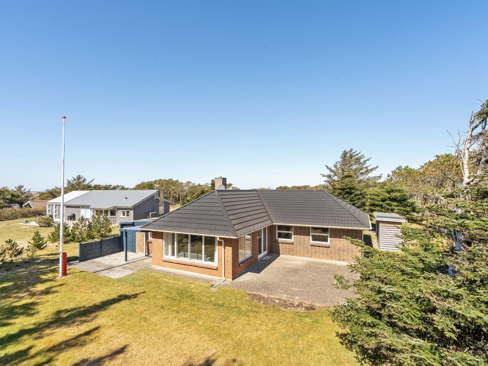 Une maison moderne à deux étages, dotée d’un toit en pente, d’une cheminée visible et d’un petit garage attenant.