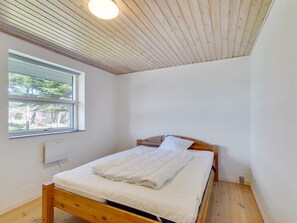 A small, neatly made room with a wooden bed, a window, and a white ceiling.
