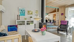 Un salon moderne avec un canapé blanc, une table basse ornée d’un vase de fleurs, une cheminée noire et, au fond, un coin repas.