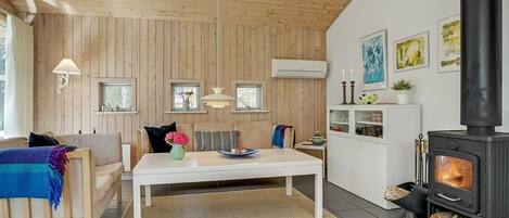 En hyggelig stue med trælofter, en sofa, et spisebord og en sort brændeovn.