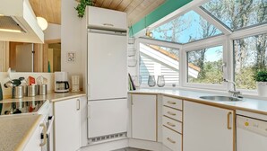 Une cuisine avec des armoires blanches, un four à micro-ondes encastré et une fenêtre donnant sur les arbres.