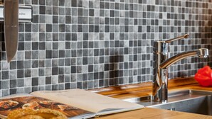 A kitchen with a tiled backsplash, a stainless steel faucet, a wooden countertop, and a red pepper.