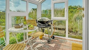 Een oranjerie met een eettafel, een barbecue en uitzicht op het omliggende groen.
