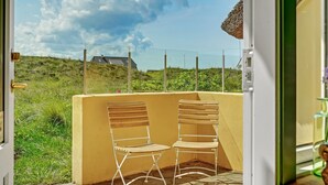 Een balkon met twee witte metalen stoelen en een gele muur, met uitzicht op een grasrijk landschap met een hek en een gebouw in de verte.