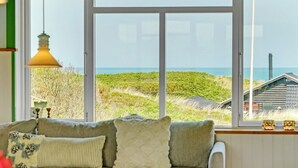 Een kamer met een groot raam met uitzicht op een strand en duinen.