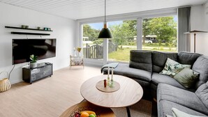 Un salon moderne avec une grande télévision, un canapé gris et une table basse ronde en bois.