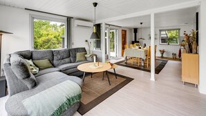 Un salon moderne avec un canapé d’angle gris, une table basse ronde et un coin repas comprenant une table et des chaises.