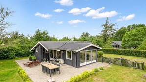 Une maison moderne dotée d’un patio, d’un coin repas et d’une grande porte vitrée donnant sur un espace extérieur abrité.