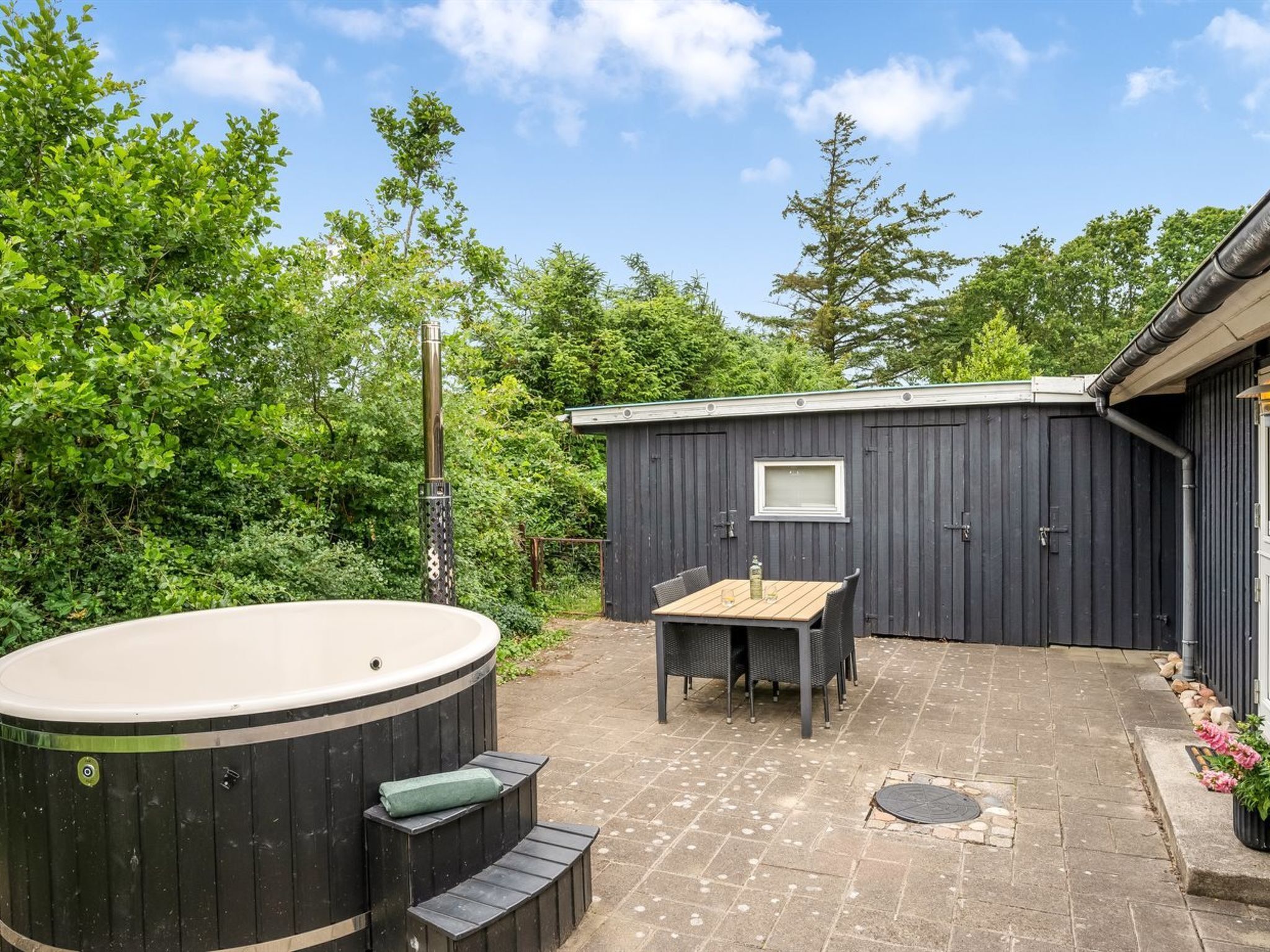 A hot tub, outdoor table, and chairs in a backyard with a wooden deck and a shed.