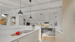 Une cuisine moderne avec des meubles blancs, un îlot central, des luminaires suspendus et une vue sur un espace de vie comprenant un canapé et une table à manger.