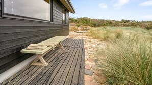 Een houten terras met een bankje en een pad van stenen dat naar een gebouw met grote ramen leidt.