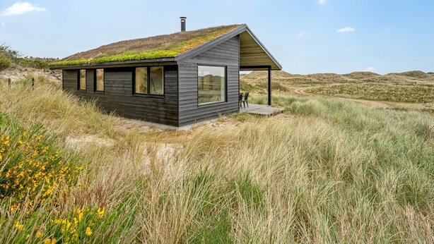 Een modern huis met een schuin dak en een groen dak, omgeven door een natuurlijke omgeving.