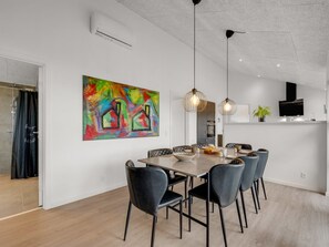 Un espace de salle à manger moderne, agrémenté d’un grand tableau abstrait, avec une cuisine en arrière-plan et une table à manger entourée de chaises.