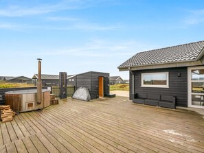 Een houten terras met een jacuzzi, een sauna en een klein gebouw met een raam.