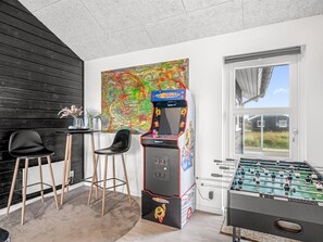 Et værelse med et fodboldbord, et barområde med barstole, et stort abstrakt maleri og et vindue med udsigt over grøn bevoksning.