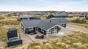 A modern house with a large deck, surrounded by a dune landscape.