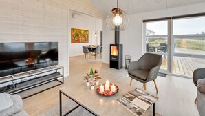 A modern living room with a TV, fireplace, dining area, and large windows overlooking the beach.