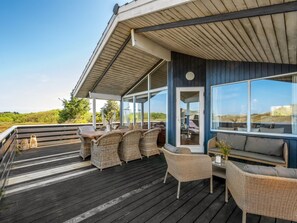 A covered outdoor deck with wicker furniture, a glass door, and a view of the landscape.