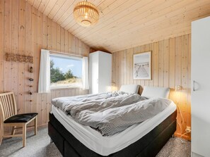 Ein Schlafzimmer mit einem Bett, einem Sessel, einem Fenster, einer Wandleuchte und einem Bild.