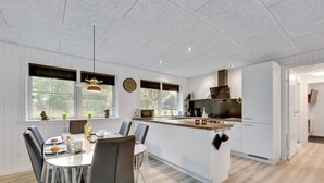 A modern kitchen with a central island, white cabinetry, and a dining area with a round table and chairs. - "Øn" -  from the sea by Interhome (Hvide Sande)