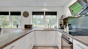 A modern kitchen with white cabinetry, a marble countertop, a built-in oven, and a large window with blinds. - "Øn" -  from the sea by Interhome (Hvide Sande)