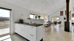A modern kitchen with a central island, a dining area with chairs, and a large window providing natural light.