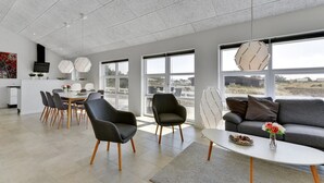 A modern living room with a dining area, large windows, and a view of the landscape.