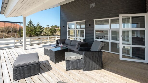 A covered outdoor deck with wicker furniture, large windows, and a view of the surrounding landscape.