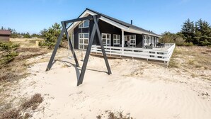 A beach house with a deck, large windows, and a swing set.